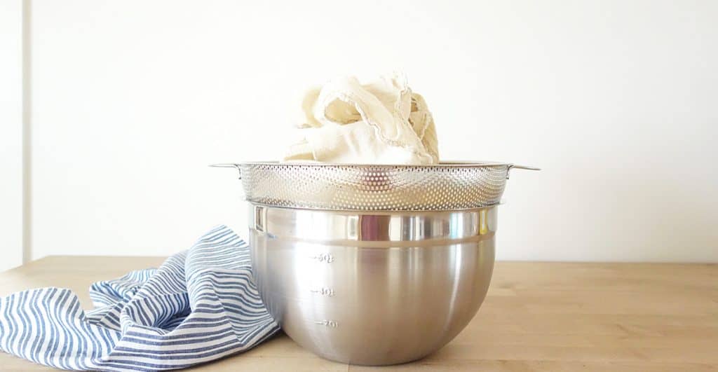 cheesecloth full of homemade yogurt in a strainer over a bowl