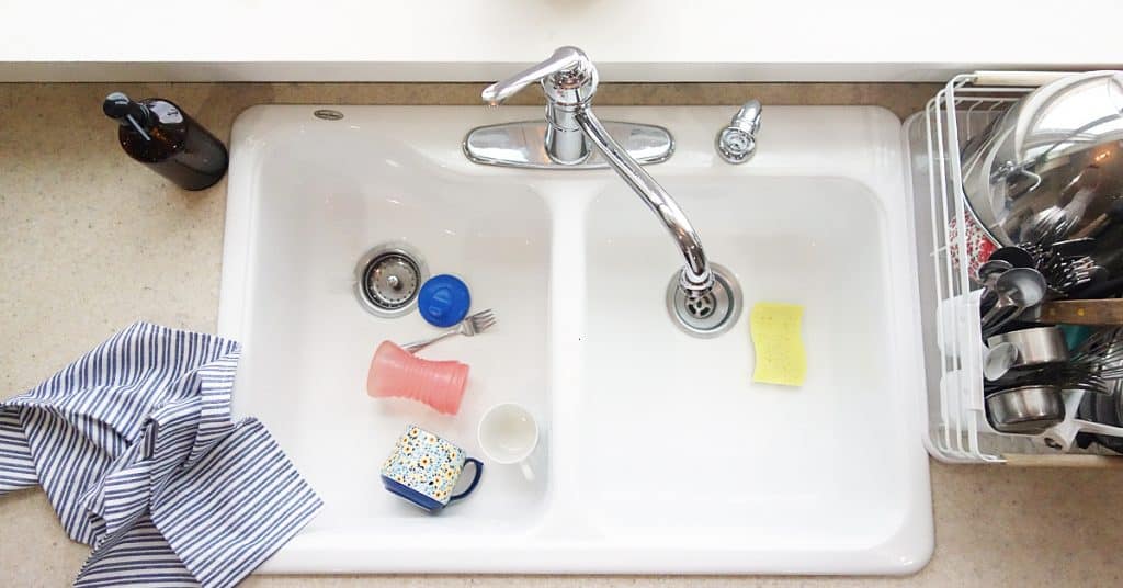 a white kitchen sink full of kids dishes. a striped towel lays on the side