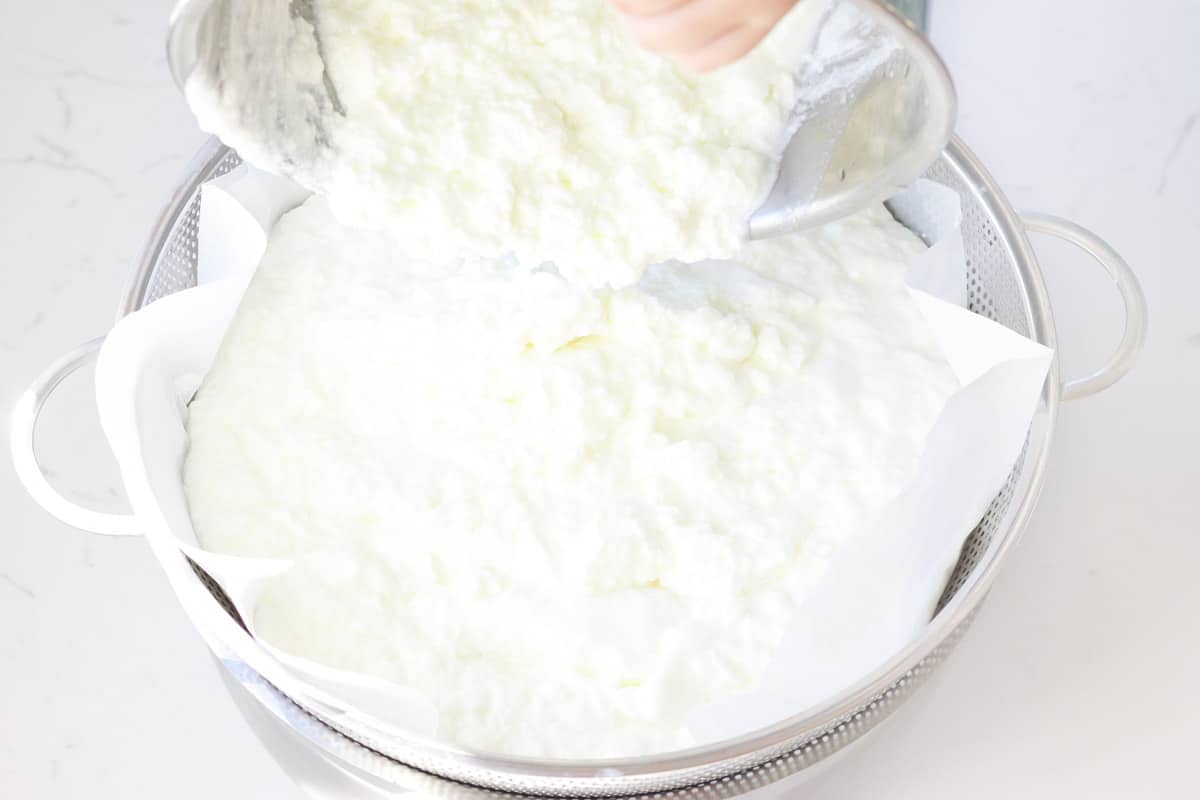 homemade yogurt being poured into a colander lined with coffee filters