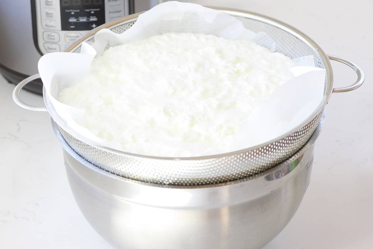 a colander set on top of a bowl, lined with coffee filters. The colander is full of homemade yogurt