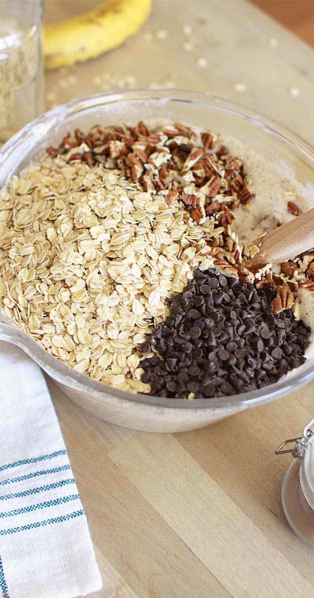 oats, chocolate chips and pecans in a mixing bowl with a wooden spoon