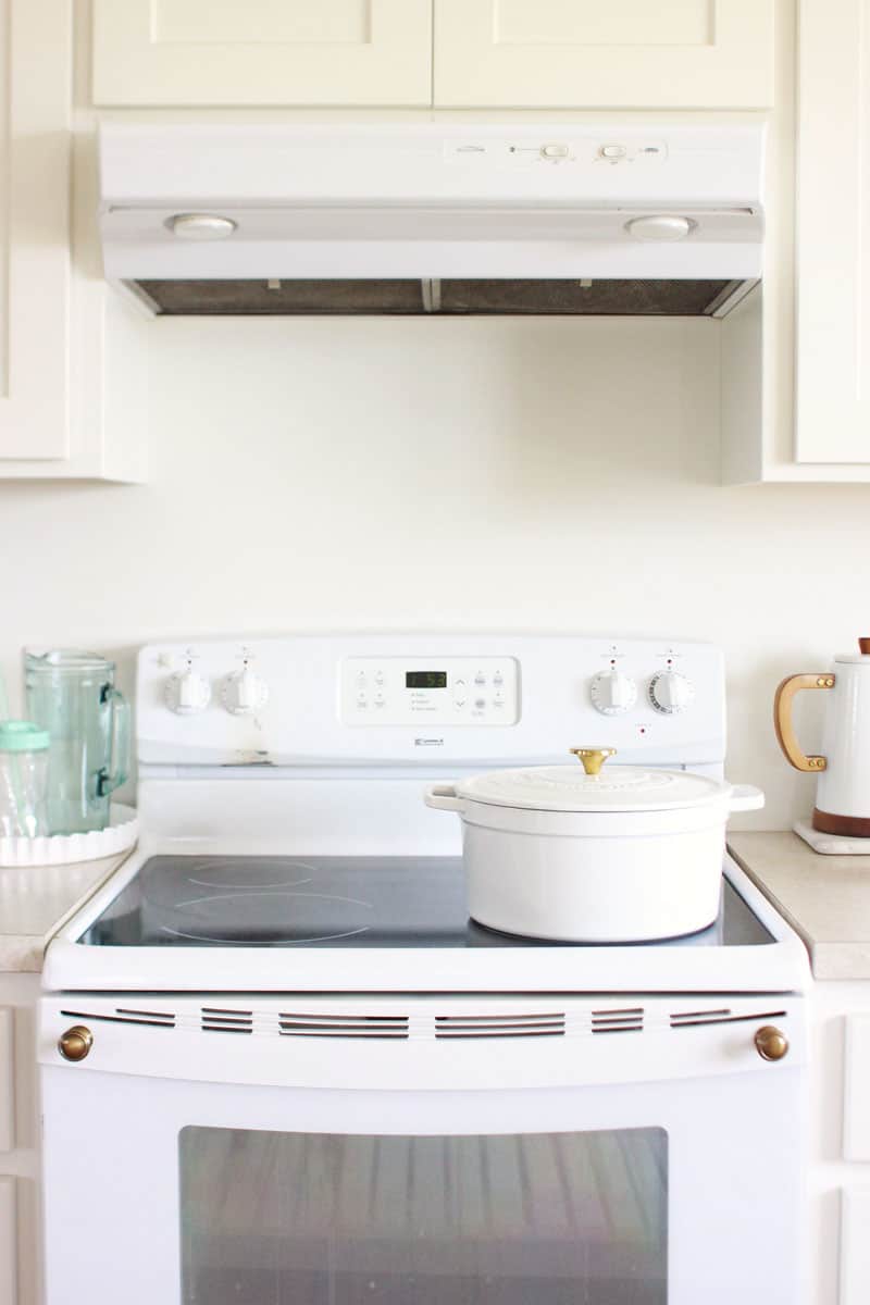 a clean shining black glass stovetop with a white Dutch oven on top and white kitchen cabinets