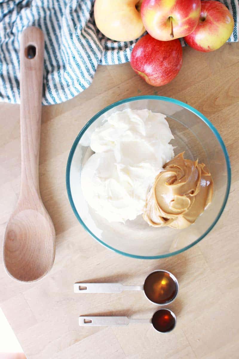 a bowl has a dollop of greek yogurt and peanut butter. a tablespoon of syrup and a teaspoon of vanilla extract