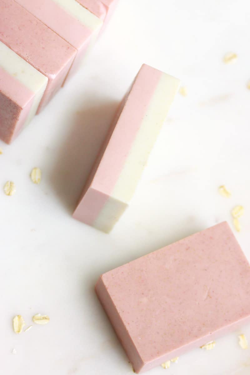 bars of pink and cream soap laying on a marble cutting board with oats sprinkled around