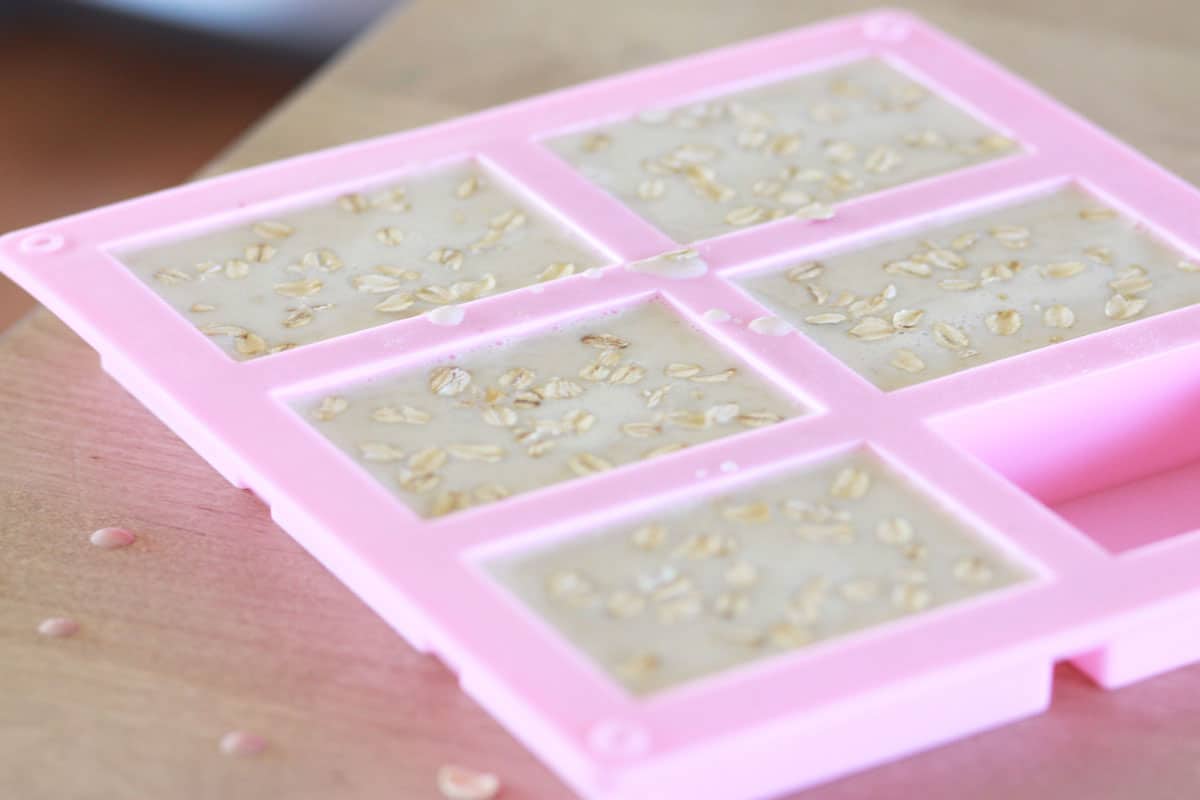 a silicone soap mold with melted soap mixture poured inside with oats on top
