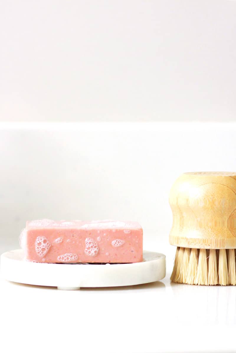 pink soap on a marble soap dish with a scrub brush next to it