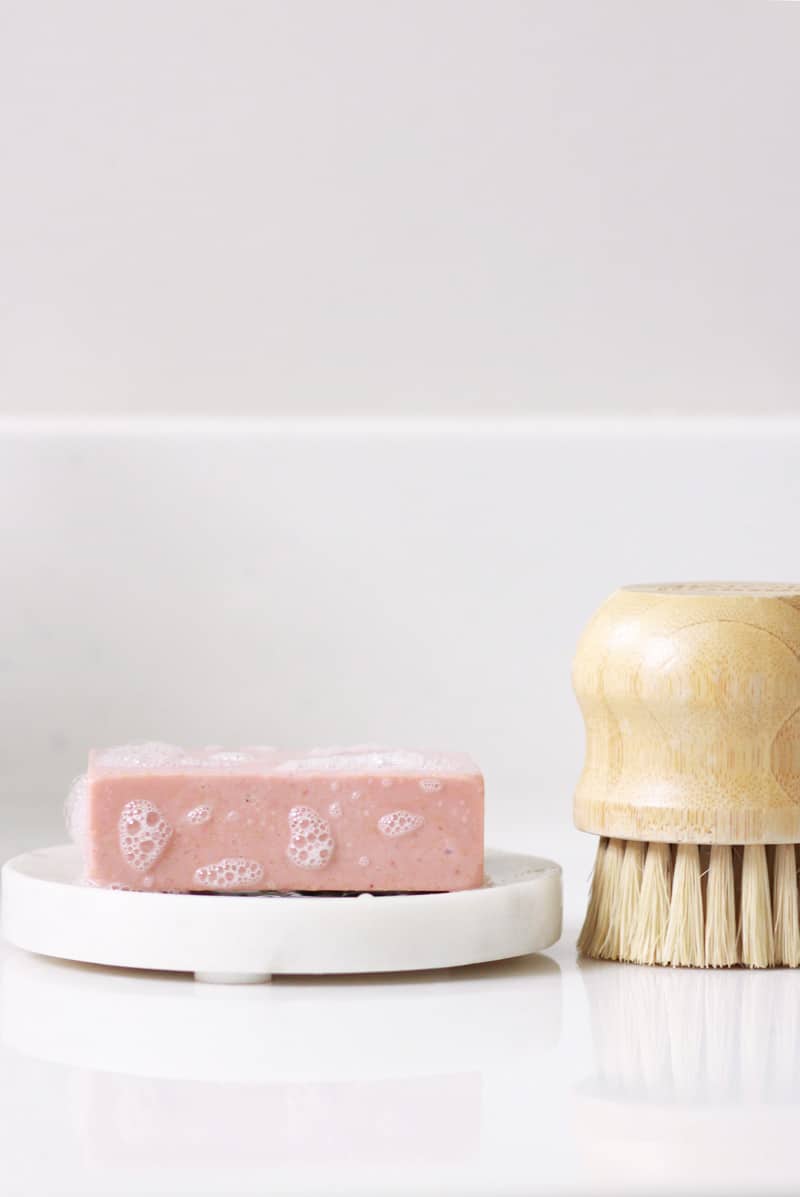 a sudsy bar of pink clay soap with a scrub brush