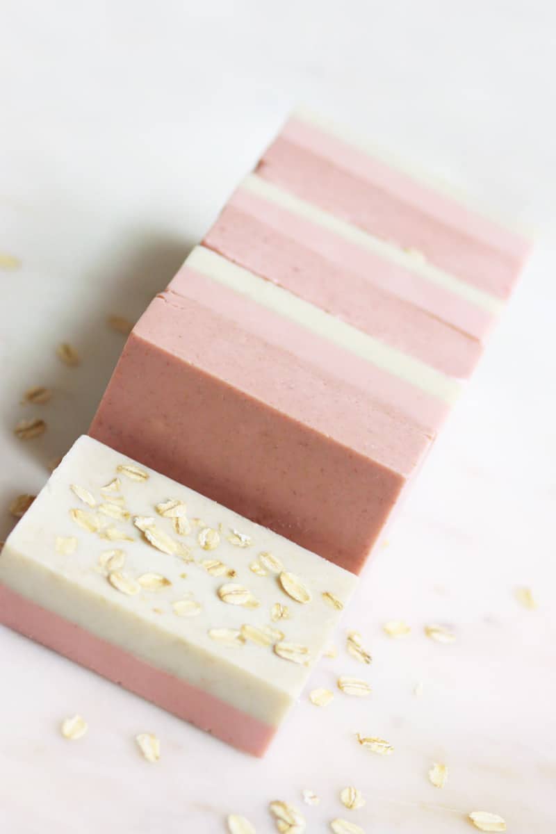 bars of pink and cream soap laying on a marble cutting board with oats sprinkled around