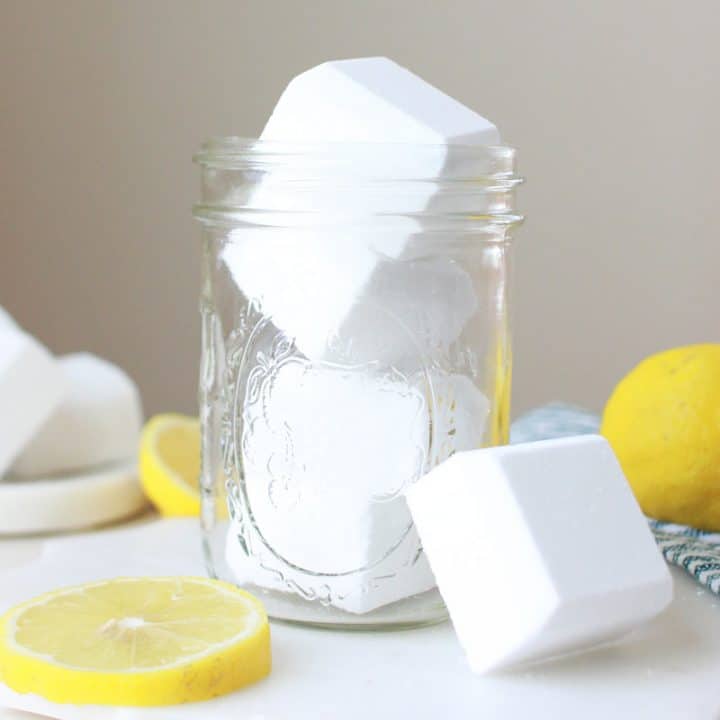 a mason jar of homemade toilet cleaner bombs and sliced lemons laying on the table around