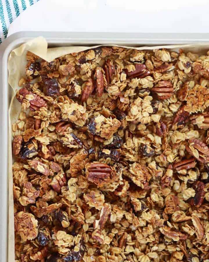 a sheet pan lined with parchment paper of homemade granola with pecans and dates in it