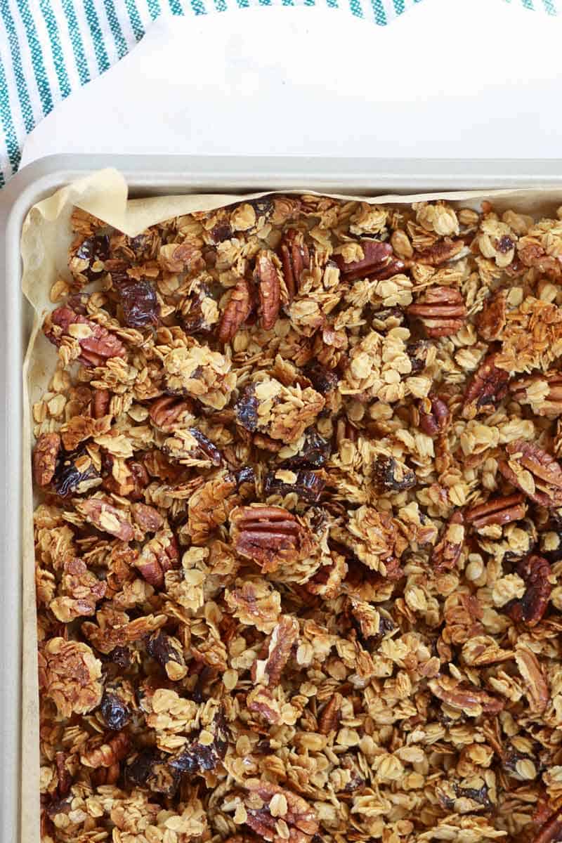 a sheet pan lined with parchment paper of homemade granola with pecans and dates in it