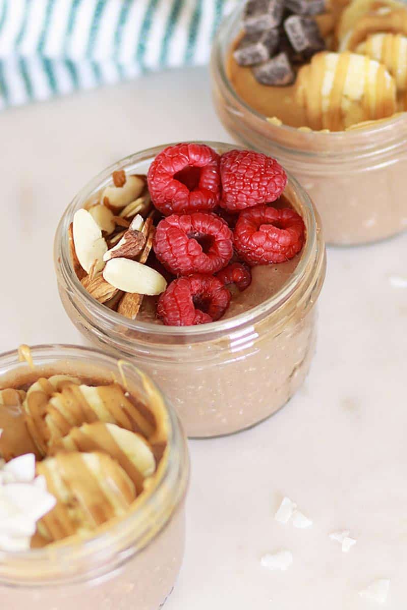 3 mason jars of chocolate overnight oats topped with raspberries and bananas