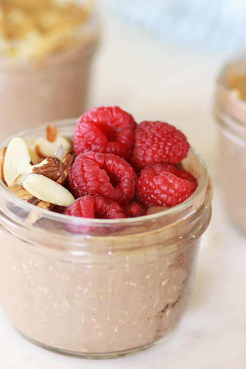 3 mason jars of chocolate overnight oats topped with raspberries and bananas