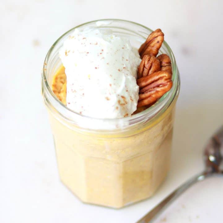 a jar of pumpkin overnight oats with whipped cream and pecans on top