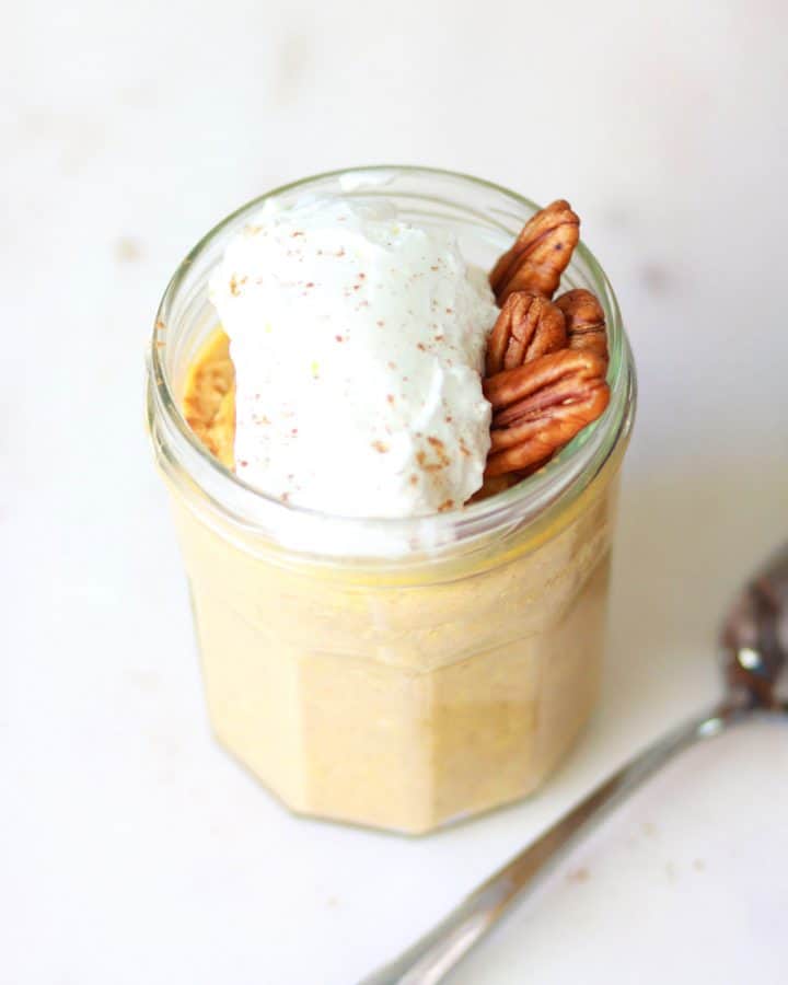 a jar of pumpkin overnight oats with whipped cream and pecans on top