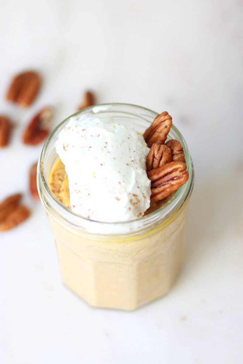 a jar of pumpkin overnight oats with whipped cream and pecans on top