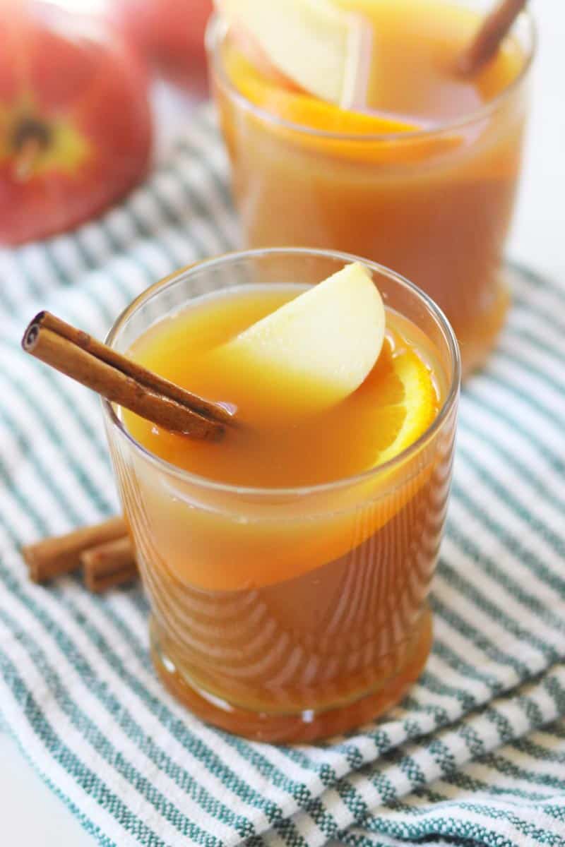 a glass with hot apple cider in it and a cinnamon stick, apple slice and orange slice in it