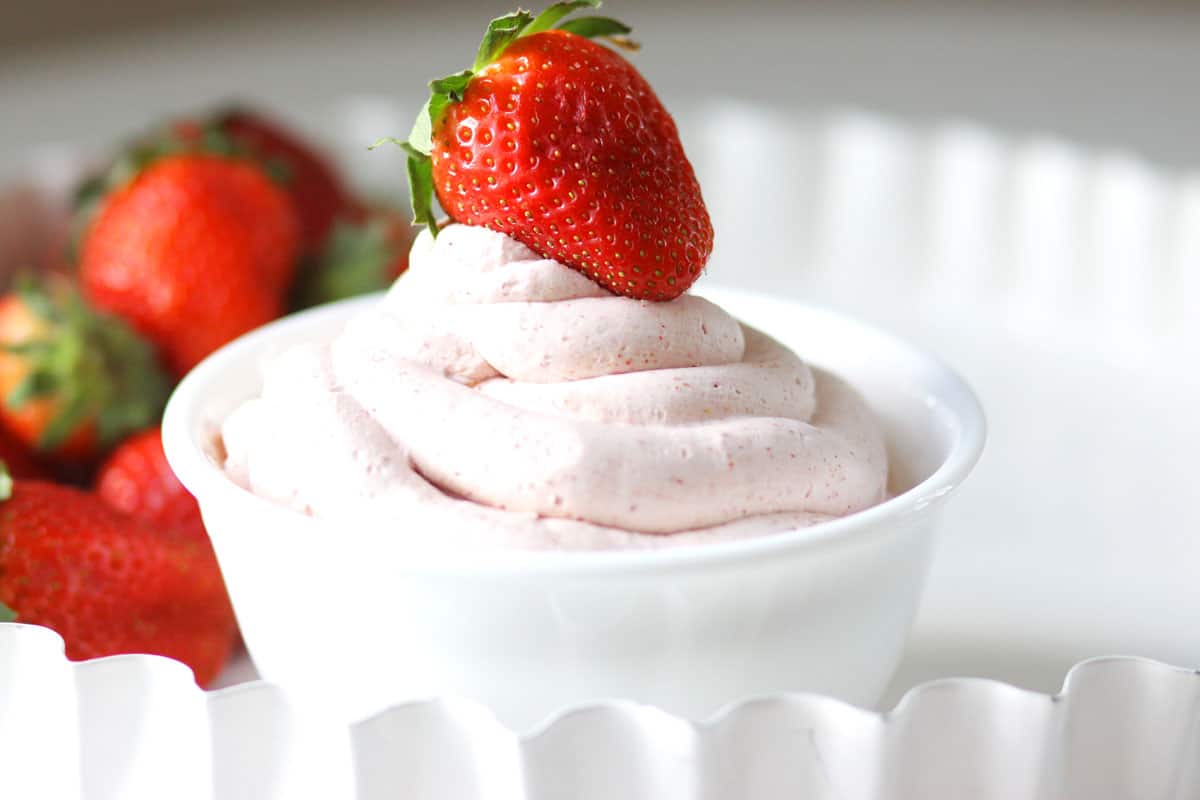 a white bowl with strawberry whipped cream in it and fresh strawberries set next to it