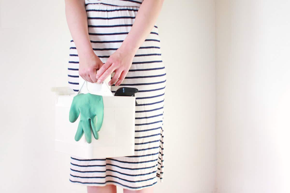 a mom holding a cleaning caddy with a green glove and spray bottle in it