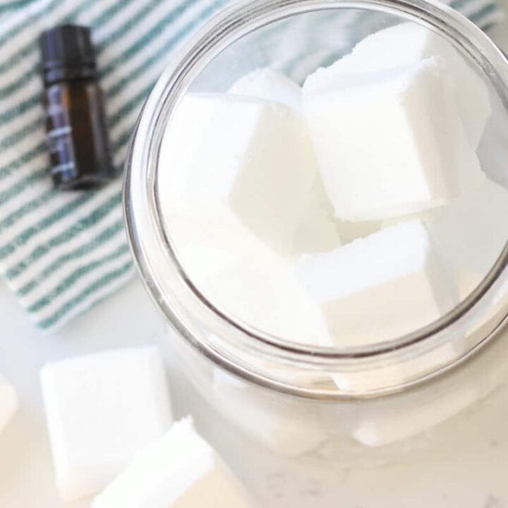 a glass canister full of toilet bowl cleaner tablets and an essential oil laying next to it