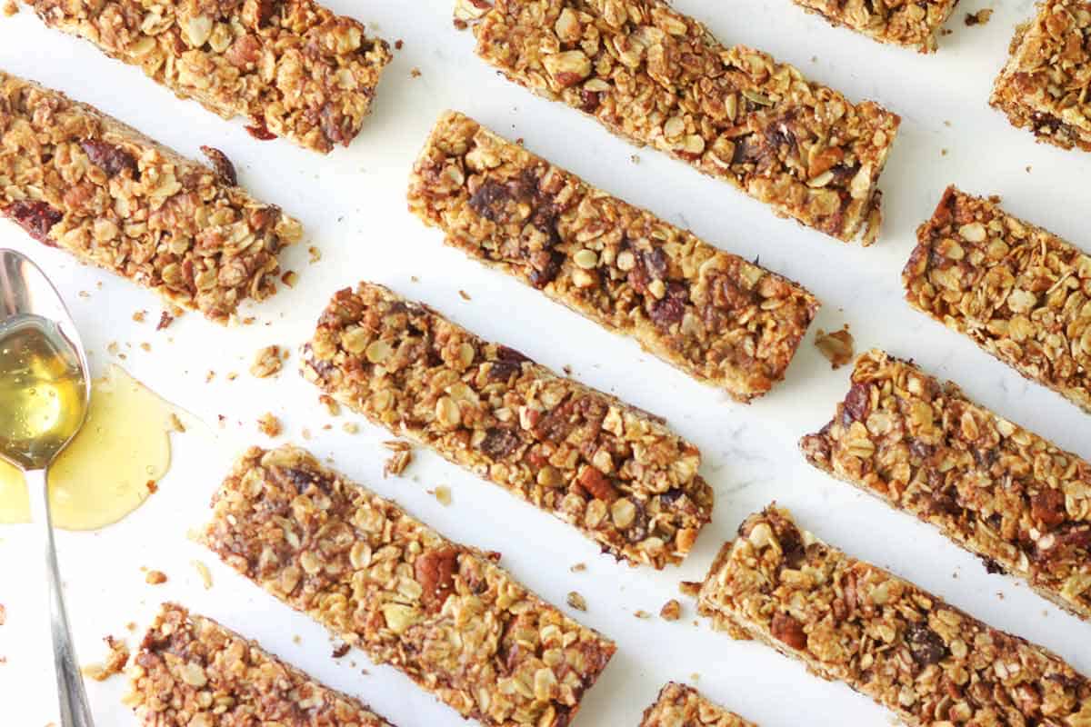 baked granola bars lined up on a marble table with a spoonful of honey next to them