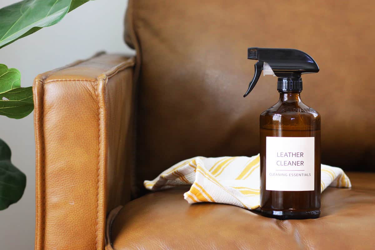 a glass amber spray bottle with a label that reads "leather cleaner". A leather couch is in the background