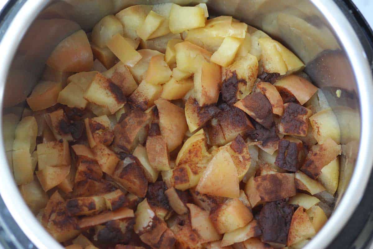 an instant pot full of cooked chopped apples with the skins on and ground cinnamon  on top