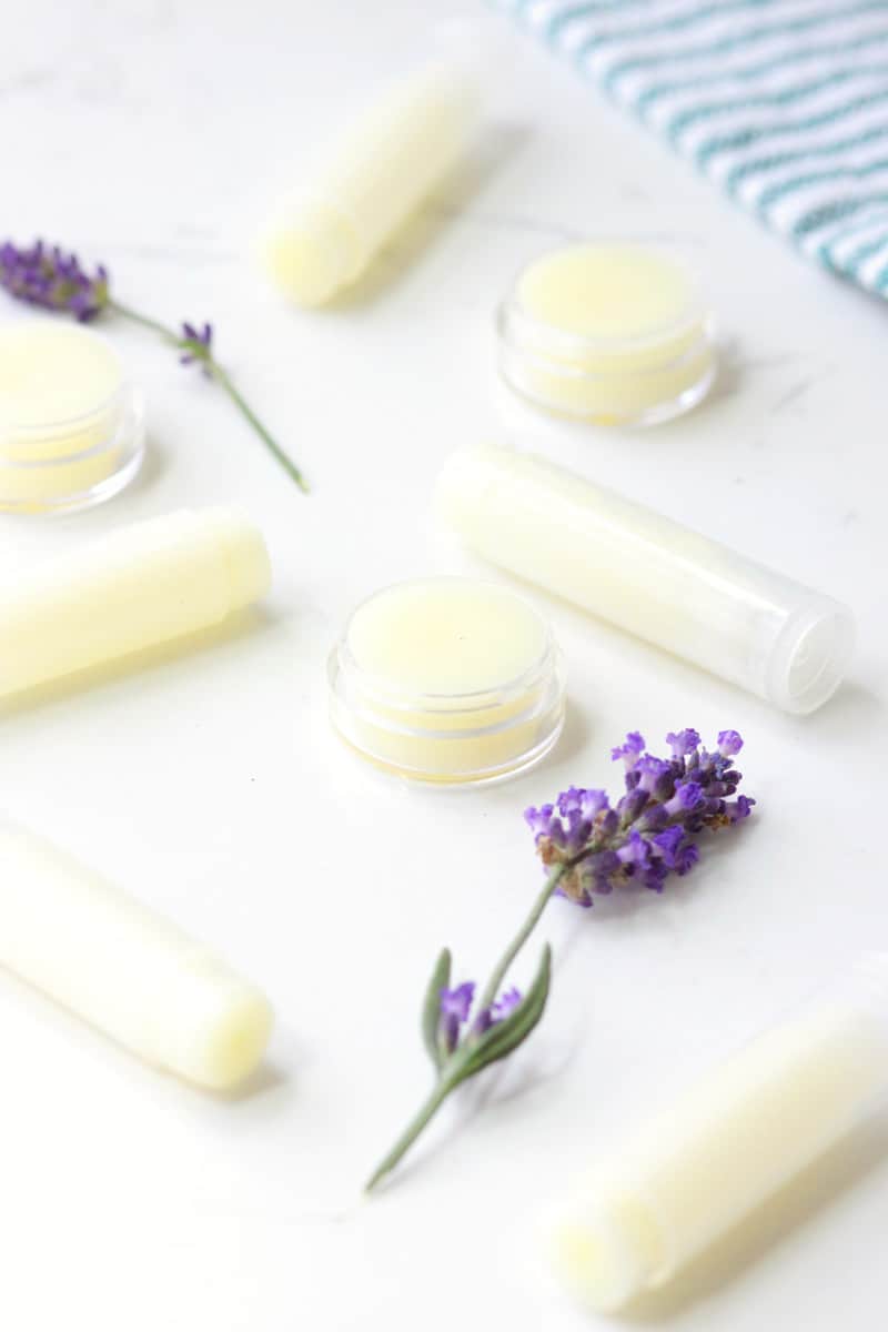 a variety of beeswax lip balms laying on a white table surrounded by lavender flowers