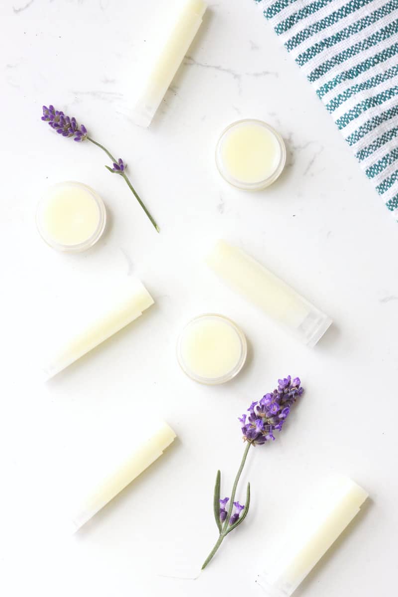 a variety of beeswax lip balms laying on a white table surrounded by lavender flowers