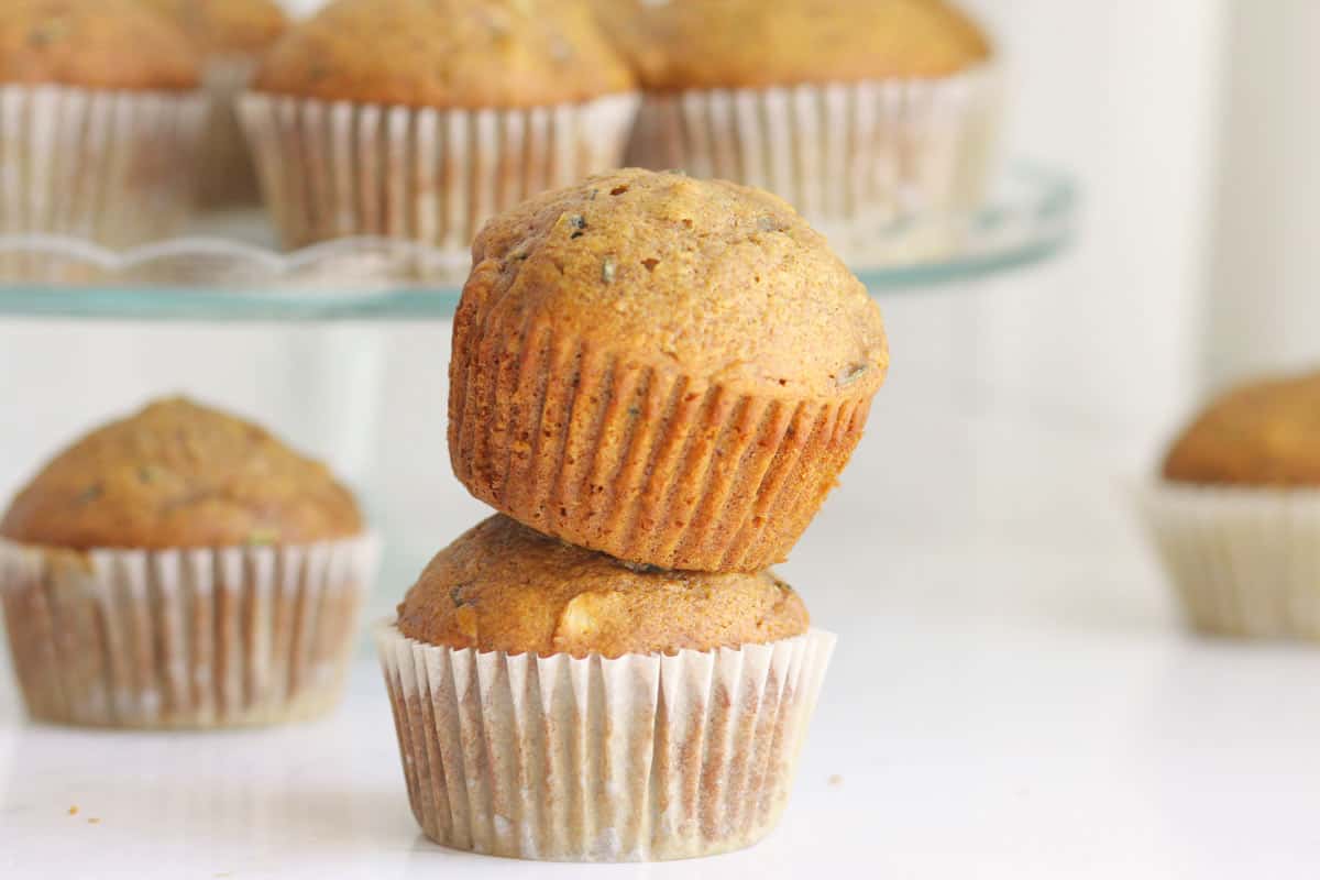 WHOLE WHEAT ZUCCHINI MUFFINS WITH APER LINERS AND A ZUCCHINI IN THE BACKGROUND