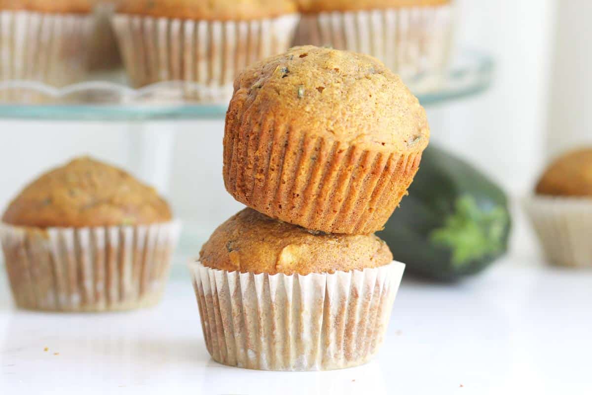 WHOLE WHEAT ZUCCHINI MUFFINS WITH APER LINERS AND A ZUCCHINI IN THE BACKGROUND