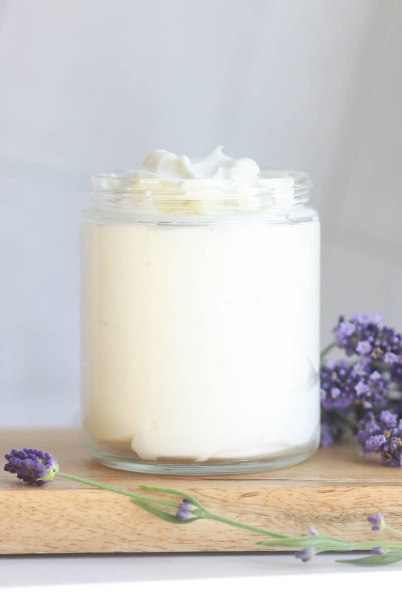 a glass jar of lotion with lavender buds laying around it