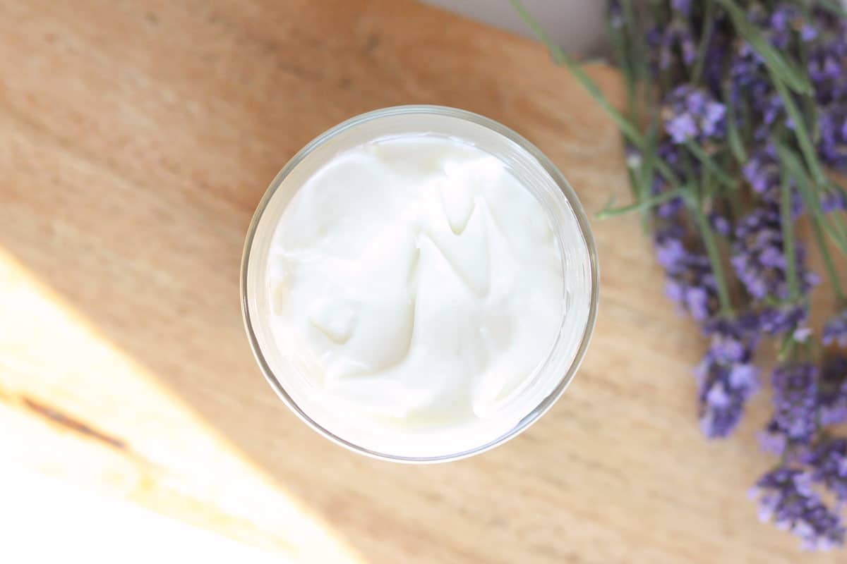 a glass jar of lotion with lavender buds laying around it