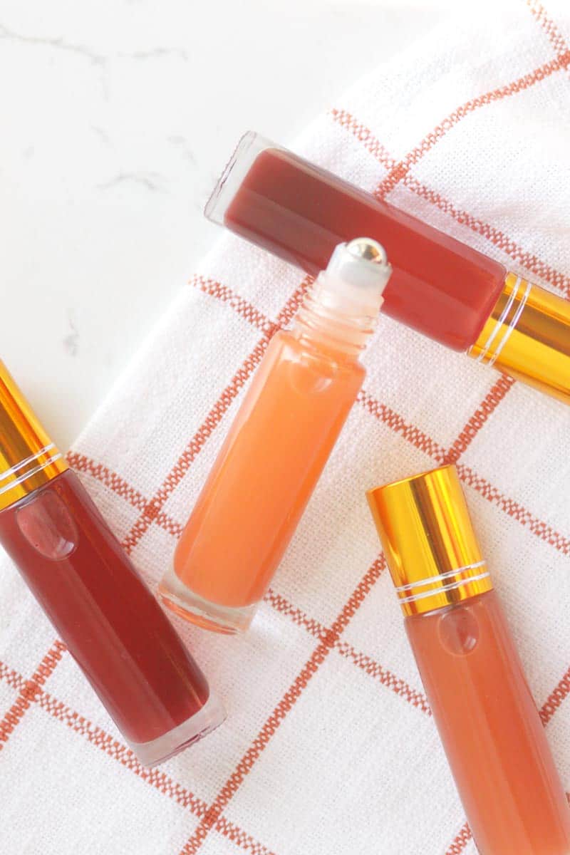 a pink lip gloss in a roller ball bottle with several bottles in the background