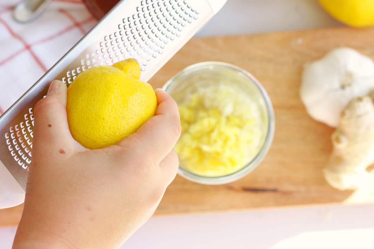 a jar of minced garlic and ginger with a hand zesting a lemon.