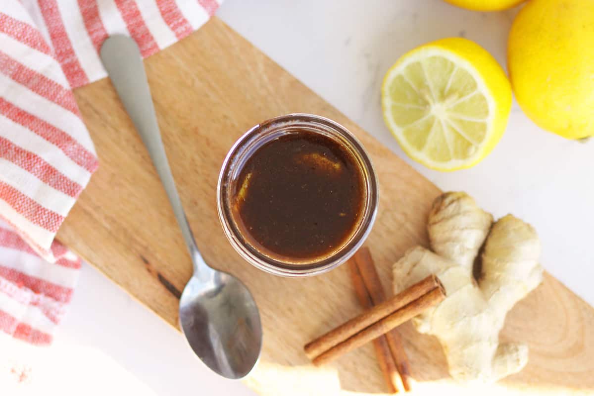 a jar full of cough syrup. A lemon, ginger and cinnamon sticks are laying next to it.