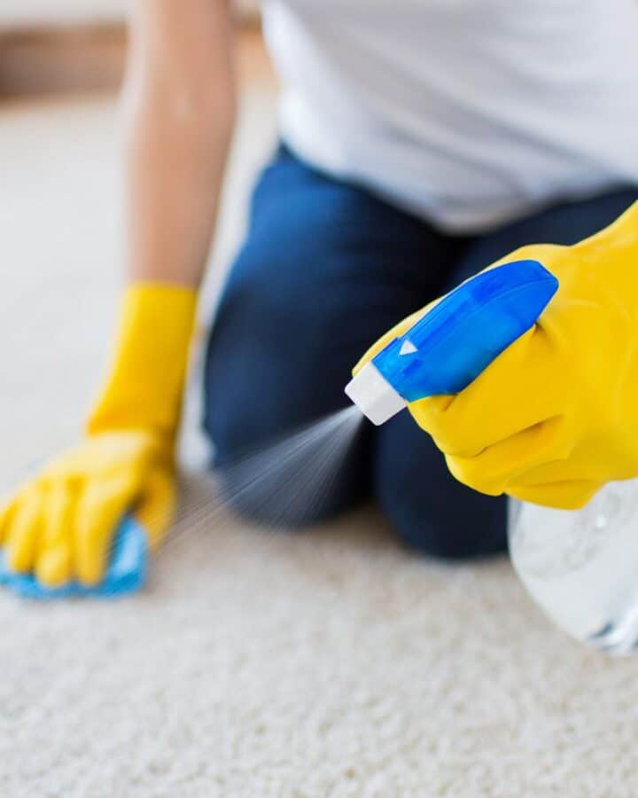a woman scrubbing carpet with a sponge and spray bottle