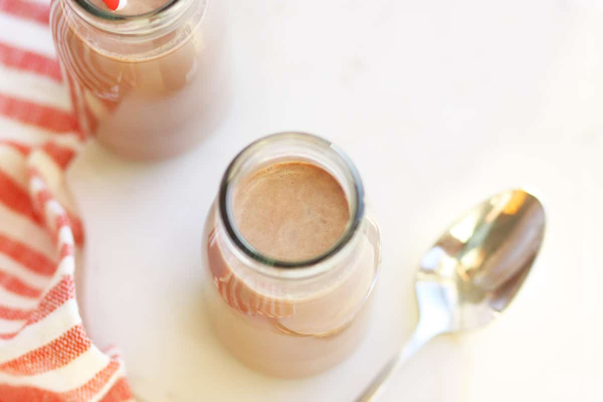 a milk bottle of frothy chocolate milk with a spoon next to it and a red and white striped towel