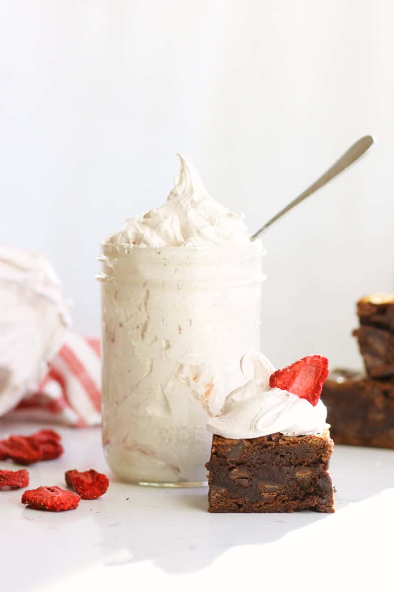 a jar of strawberry marshmallow fluff with a brownie next to it with marshmallow fluff and a freeze dried strawberry on top