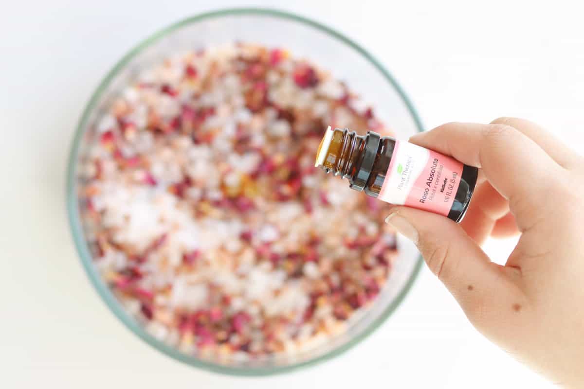 drops of rose essential oil being added to a bowl of sea salt, Himalayan pink salt and rose petals to make bath salts