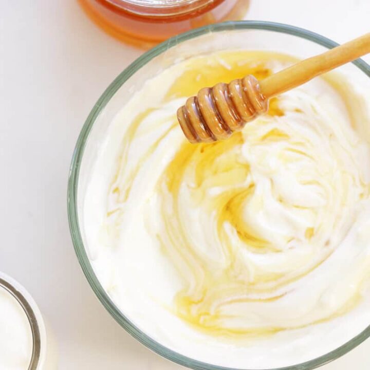a bowl of yogurt with honey swirled into it and a honey stir stick resting over it