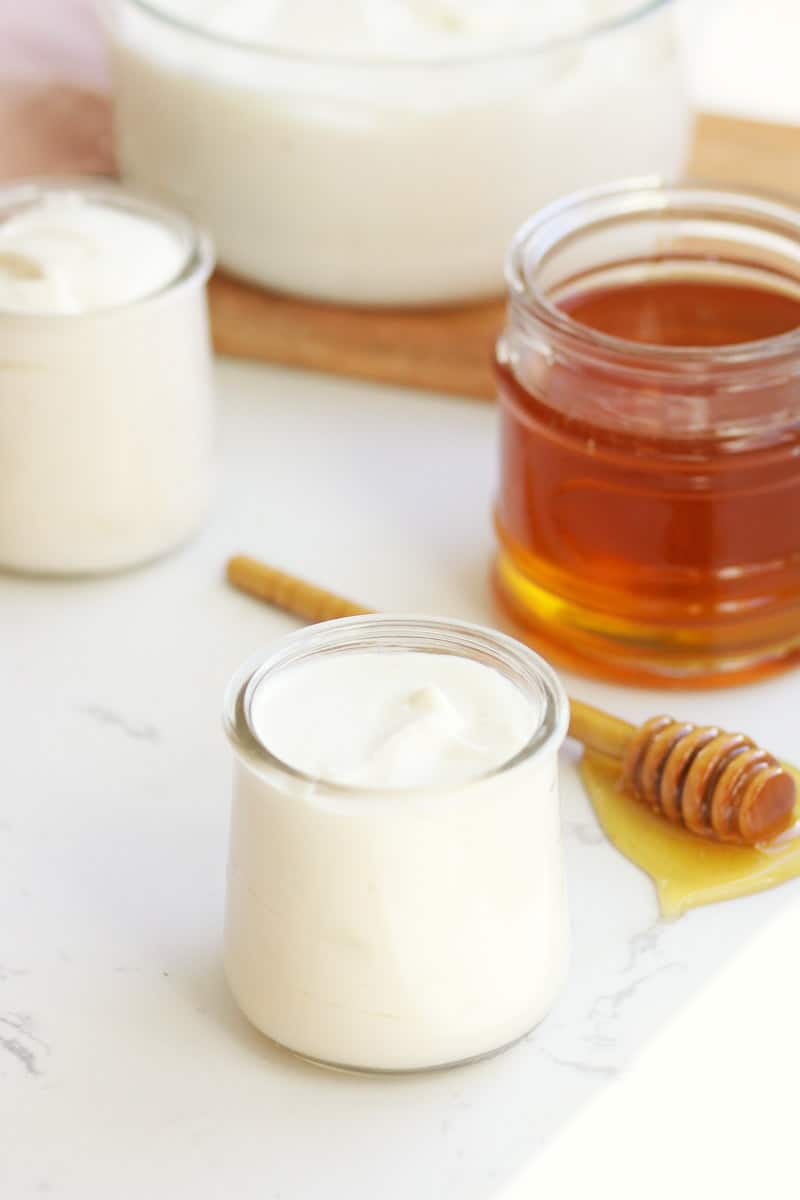 a small glass jar of yogurt with a jar of honey and a honey stir stick laying next to it