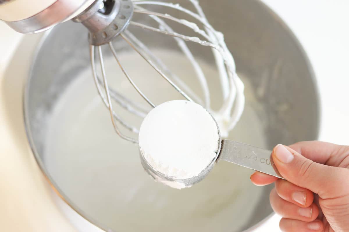 a cup measure of zinc oxide powder being added to a mixer with homemade sunscreen in it