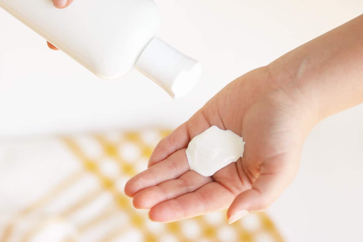 a bottle of sunscreen being squeezed into a hand. A yellow and white striped towel is behind.