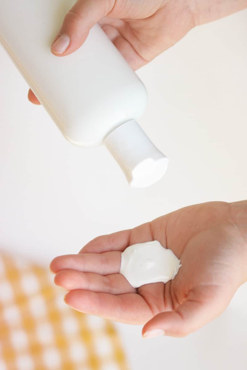 a bottle of sunscreen being squeezed into a hand. A yellow and white striped towel is behind.