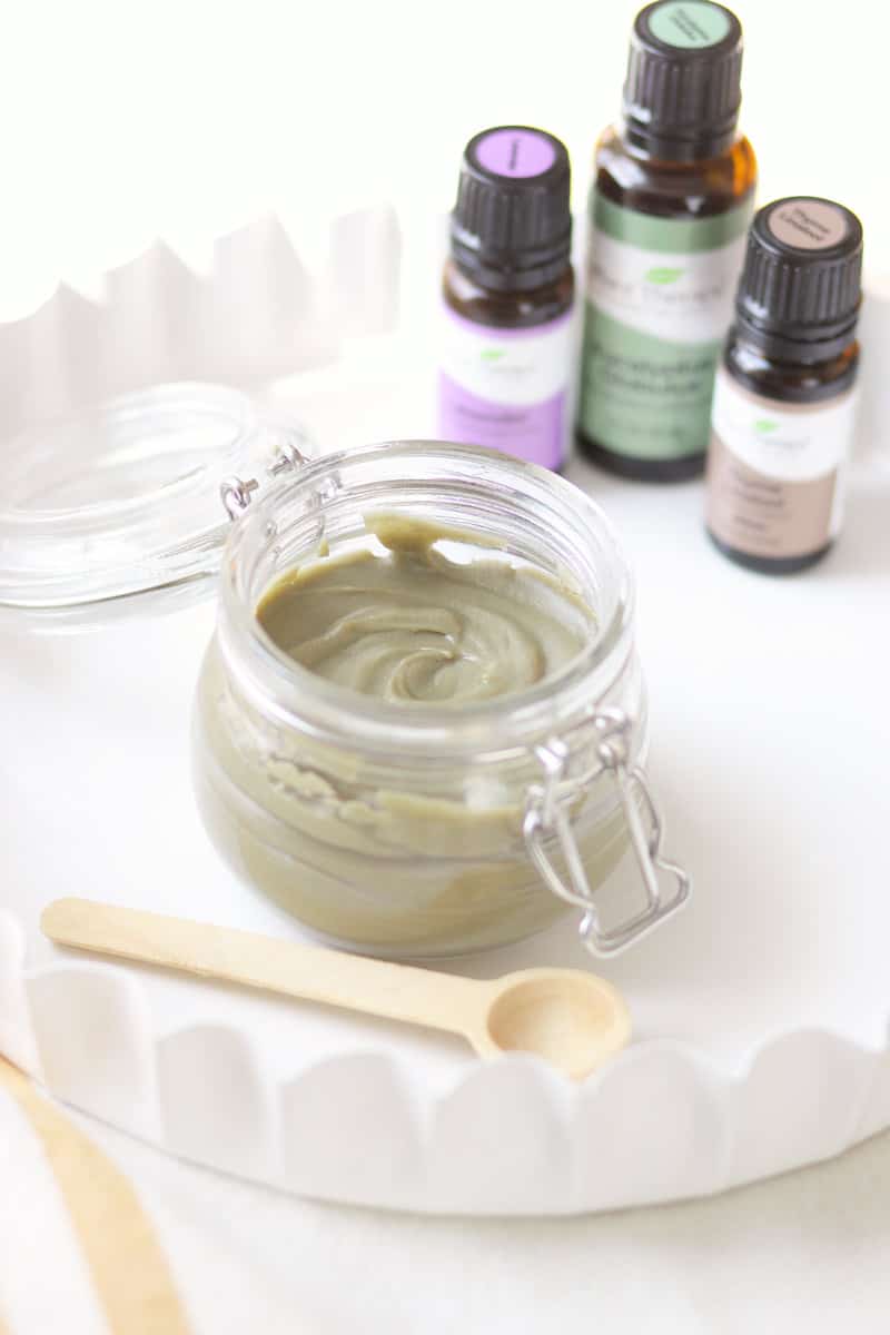 a jar of homemade anti-itch cream with essential oils behind it