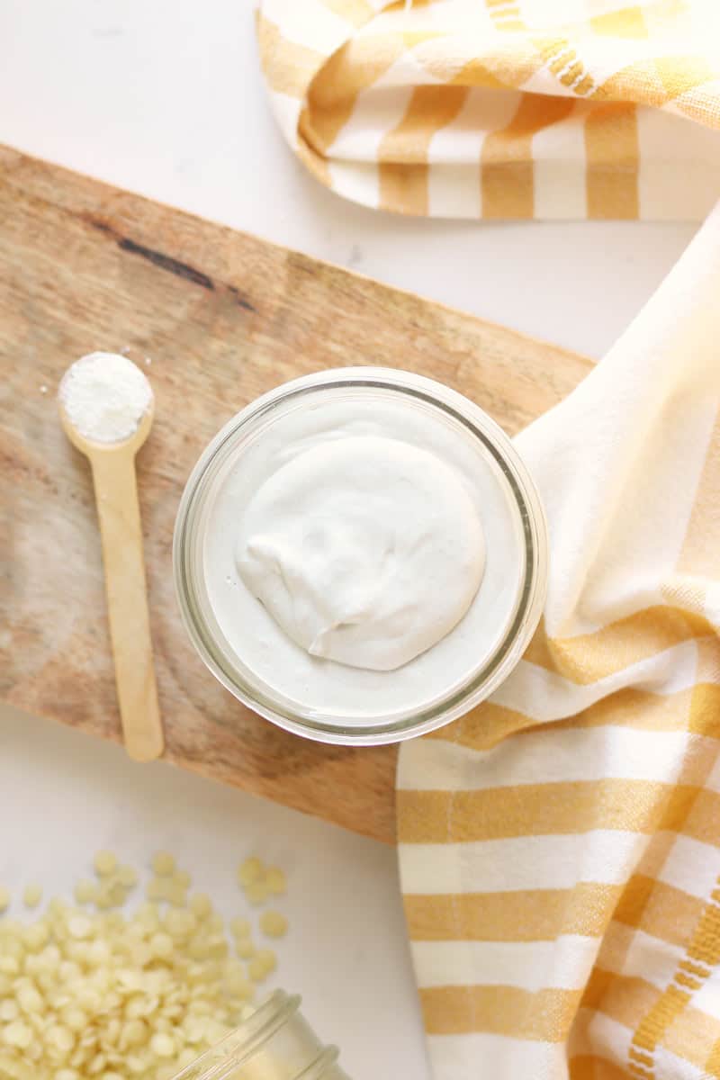 a jar of homemade diaper rash cream with dried lavender flowers and a spoonful of zinc oxide next to it on a wooden cutting board