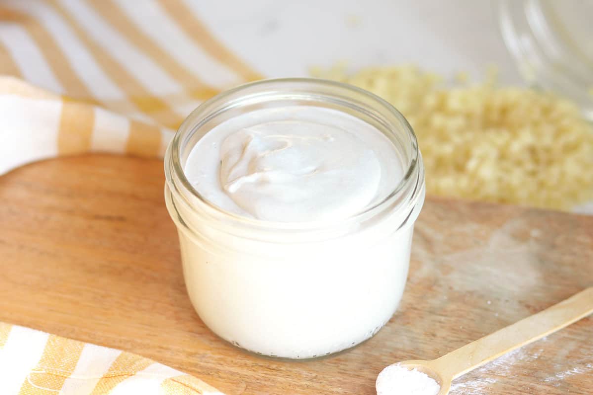 a jar of homemade diaper rash cream with dried lavender flowers and a spoonful of zinc oxide next to it on a wooden cutting board