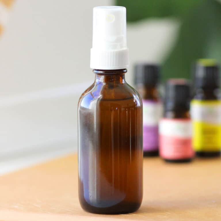 a small glass amber spray bottle with essential oils on the table behind it