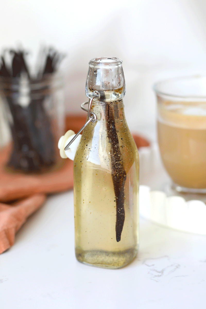 A glass bottle of vanilla syrup with a whole fresh vanilla bean in it